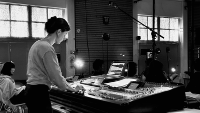 Une femme devant une console de son, créant de la musique électronique dans un studio.