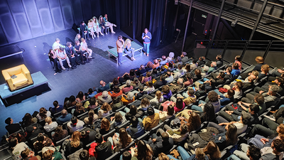 Treize étudiants sur scène, jouant dans une salle de spectacle pleine.