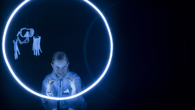 Une jeune femme dans le noir, entourée d'un cercle lumineux. À côté d'elle, pendent un masque et des gants de plongée.