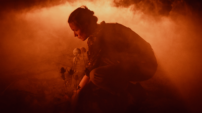 Une femme plante une fleurs, entourée de fumée rouge.