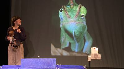 Une femme montre à une marionnette d'enfant un écran avec un caméléon dessus.
