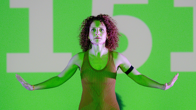 Une danseuse devant un écran vert avec le nombre "151" inscrit dessus.