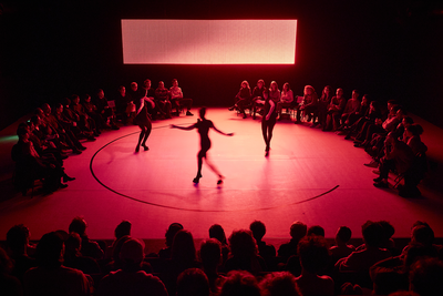 Trois danseuses vêtues de pieds de boucs au centre d'une scène. La lumière est rouge.