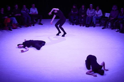 Trois danseuses vêtues de pieds de boucs au centre d'une scène. La lumière est violette.