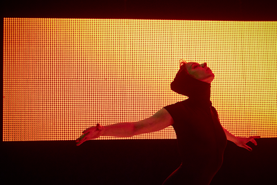 Une danseuse devant un écran lumineux orange.