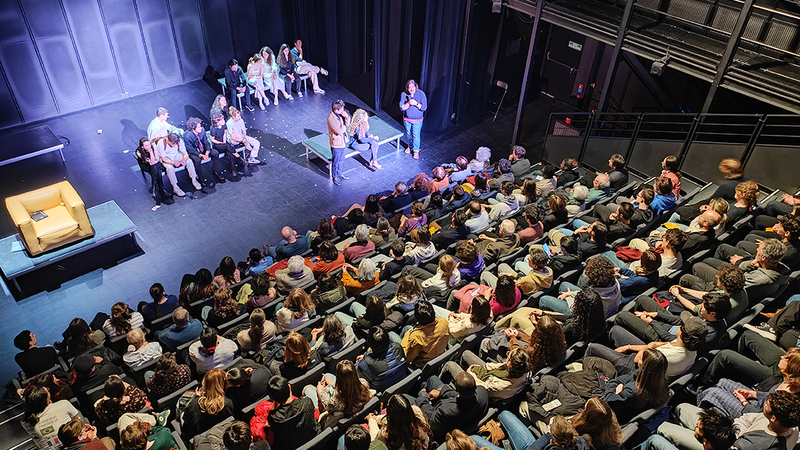 Treize étudiants sur scène, jouant dans une salle de spectacle pleine.